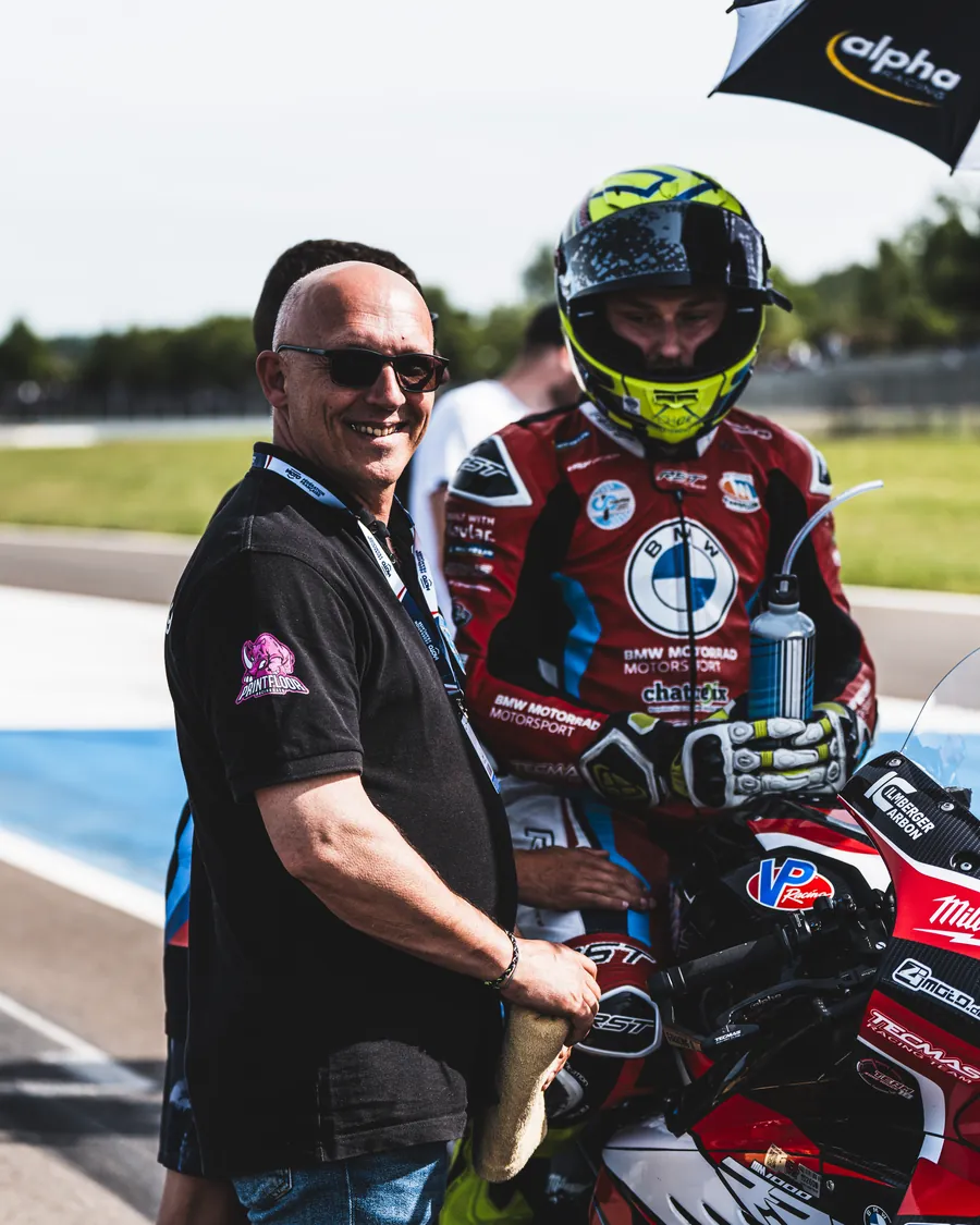 Philippe Ciminera souriant aux côtés d'un pilote BMW sur sa moto, en bord de piste